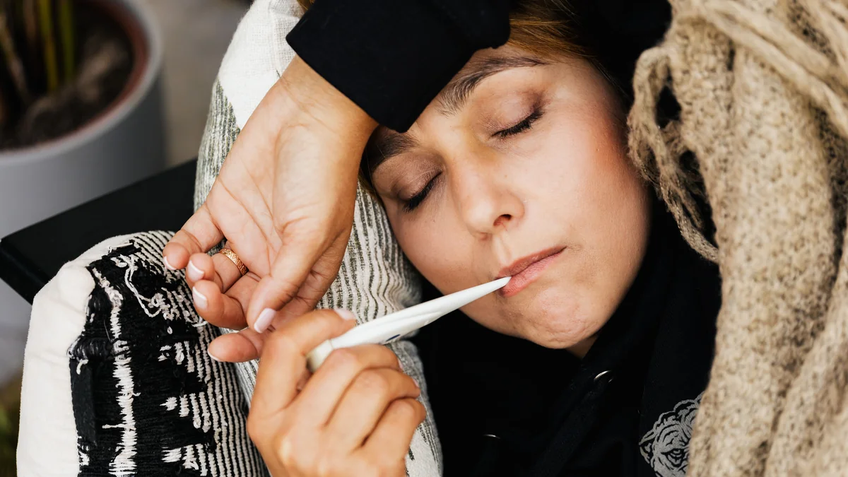 Person med filt och termometer vilar i soffan
